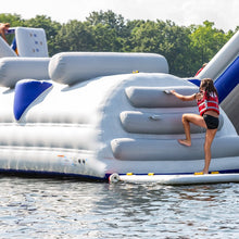 Person climbing onto a large inflatable structure in the water with trees in the background
