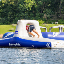Person on an inflatable water obstacle course in a lake with trees and grass in the background