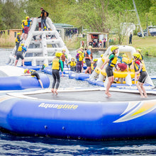 Children playing on an inflatable water playground with 'Aquaglide' branding in a park setting.