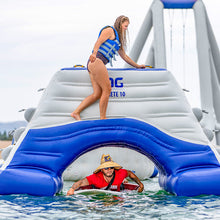 Woman on an inflatable water slide with a man in the water below, on a cloudy day.