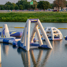 Inflatable water park structures on a lake with grassy area and trees in the background.