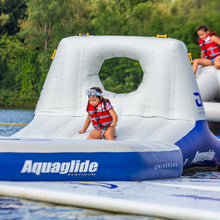 Child on an inflatable water toy with 'Aquaglide' branding near a body of water.