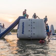 Inflatable water slide with children playing on a lake at sunset.