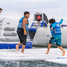Two children in life vests on an inflatable water park structure.