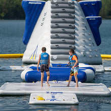 Two children on inflatable platforms with a large inflatable water slide in the background.