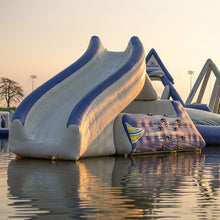 Inflatable water slide structure on a body of water with a sunset sky.