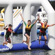 Three children in life vests jumping off an inflatable water slide into a body of water.