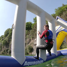 Person in a wetsuit climbing an inflatable water slide with 'Aquaglide' branding.