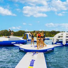People on inflatable water platforms in a pool with a clear blue sky.