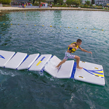 Person on an inflatable water obstacle course in a body of water with people in the background.