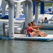 Two people on an Aquaglide Solarium  taking a selfie with more inflatables in the background.