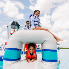 Children playing on an inflatable structure at a water park with a clear blue sky.