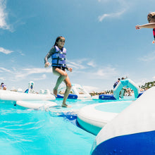 Child playing on an inflatable water toy in a pool with a clear blue sky.