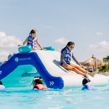 Children playing on an inflatable water slide at a pool with clear blue sky and palm trees in the background.