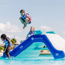 Children playing on an inflatable water slide with 'Penguin Plunge' branding in a pool.