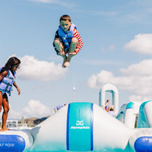 Child in a life jacket jumping off an inflatable water slide with 'Aquaglide' branding.