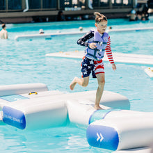 Child running on floating platforms in a pool with a scenic background