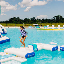 Person on a floating platform in a pool with inflatable toys and people in the background