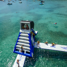 Inflatable water slide in the middle of a clear blue sea with people around it.