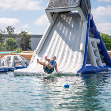 Person sliding down an inflatable water slide into a pool on a sunny day.