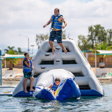 Two people on an inflatable water obstacle course in a pool