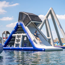 Inflatable water slide with a person sliding down, set against a clear blue sky.