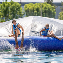 Two children playing on a large inflatable slide in a water park with trees in the background.