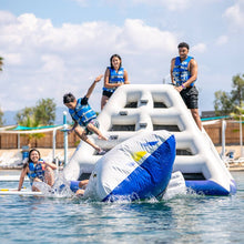 Four people on an inflatable water slide in a pool with a clear sky.