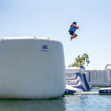 Person jumping off an inflatable obstacle into water with clear blue sky.