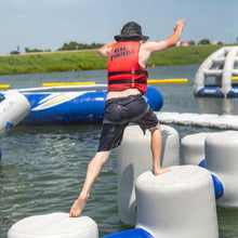 Person in a life jacket jumping from an inflatable platform into water with more platforms and people in the background.
