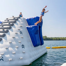 Inflatable water park with a person jumping off a blue platform into a lake.