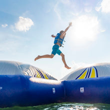 Person in a blue life jacket jumping off a large inflatable water slide into water.