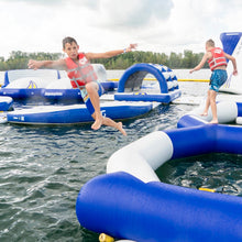 Children playing on inflatable water toys in a body of water with trees in the background.