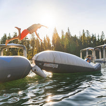 Person jumping off an inflatable structure into a body of water with trees in the background