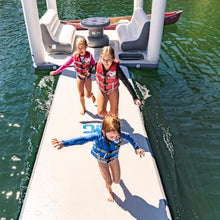 Three children in life vests standing on Full Deck with a boat in the background.