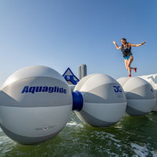 Person jumping between large white Aquaglide branded obstacles on water.