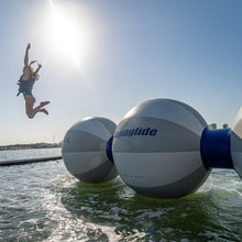 Person jumping off a large inflatable ball labeled 'Aquaglide' into water.
