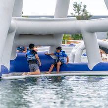 Two people on a blue inflatable tube in a pool with white arches.