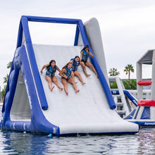 Inflatable water slide with children on a body of water, surrounded by palm trees.