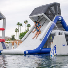 Two people sliding down an inflatable water slide with Aquaglide branding in a pool.