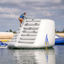 Person on an inflatable water obstacle course in a body of water with a cloudy sky.