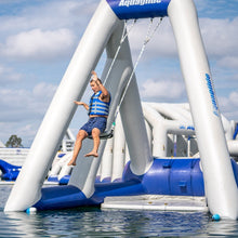 Person on an inflatable water slide with 'Aquaglide' branding, set against a blue sky and water background.