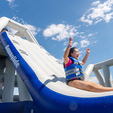 Person sliding down an inflatable water slide with a blue and white slide and clear sky.