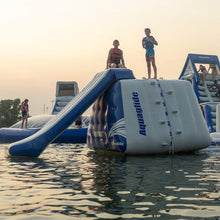 Inflatable water park with slide and climbing wall on a lake at sunset.