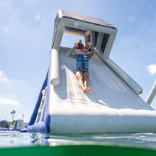 Person sliding down a large inflatable water slide in a pool with a clear blue sky.