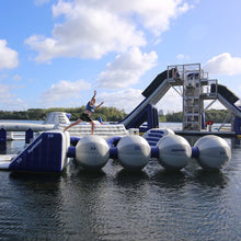 Person on an inflatable water obstacle course with 'Aquaglide' branding over a body of water.