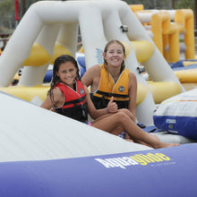 Two children in life vests sitting on an inflatable water slide with 'Aquaglide' branding.