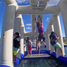 People on an inflatable water park structure with a clear blue sky.