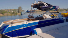 A blue and white wakeboard boat docked outdoors near water with a Island Hopper Inflatable Bull Shark Bumper Fender