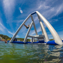Person swinging on a large inflatable structure in a body of water under a blue sky.